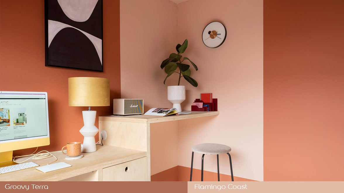 Stijlvolle thuiswerkplek met perzikkleurige muren, bureau met computer, gele tafellamp en wandplank met plant en decoraties