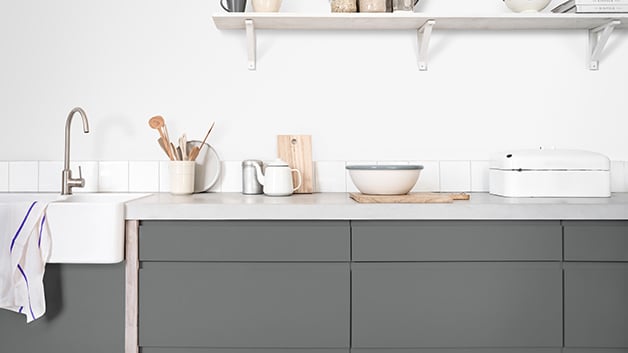 Een moderne keuken met grijze kasten, een wit aanrechtblad en netjes gerangschikte keukengerei en kommen.
