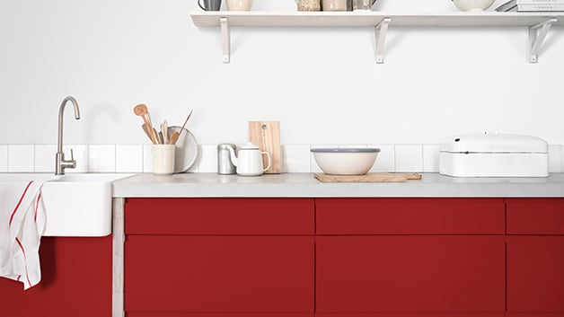 Een moderne keuken met rode kasten, een wit aanrechtblad en netjes gerangschikt keukengerei en kommen.