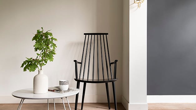 Een moderne minimalistische kamer met een zwarte stoel, een witte salontafel en een vaas met groene bladeren.