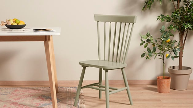 Een lichtgroene houten stoel naast een eettafel en een kamerplant in een gezellige ruimte.