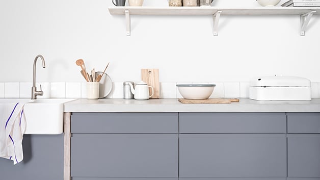 Een moderne keuken met grijze kasten, een wit aanrechtblad en netjes gerangschikte keukengerei en kommen.