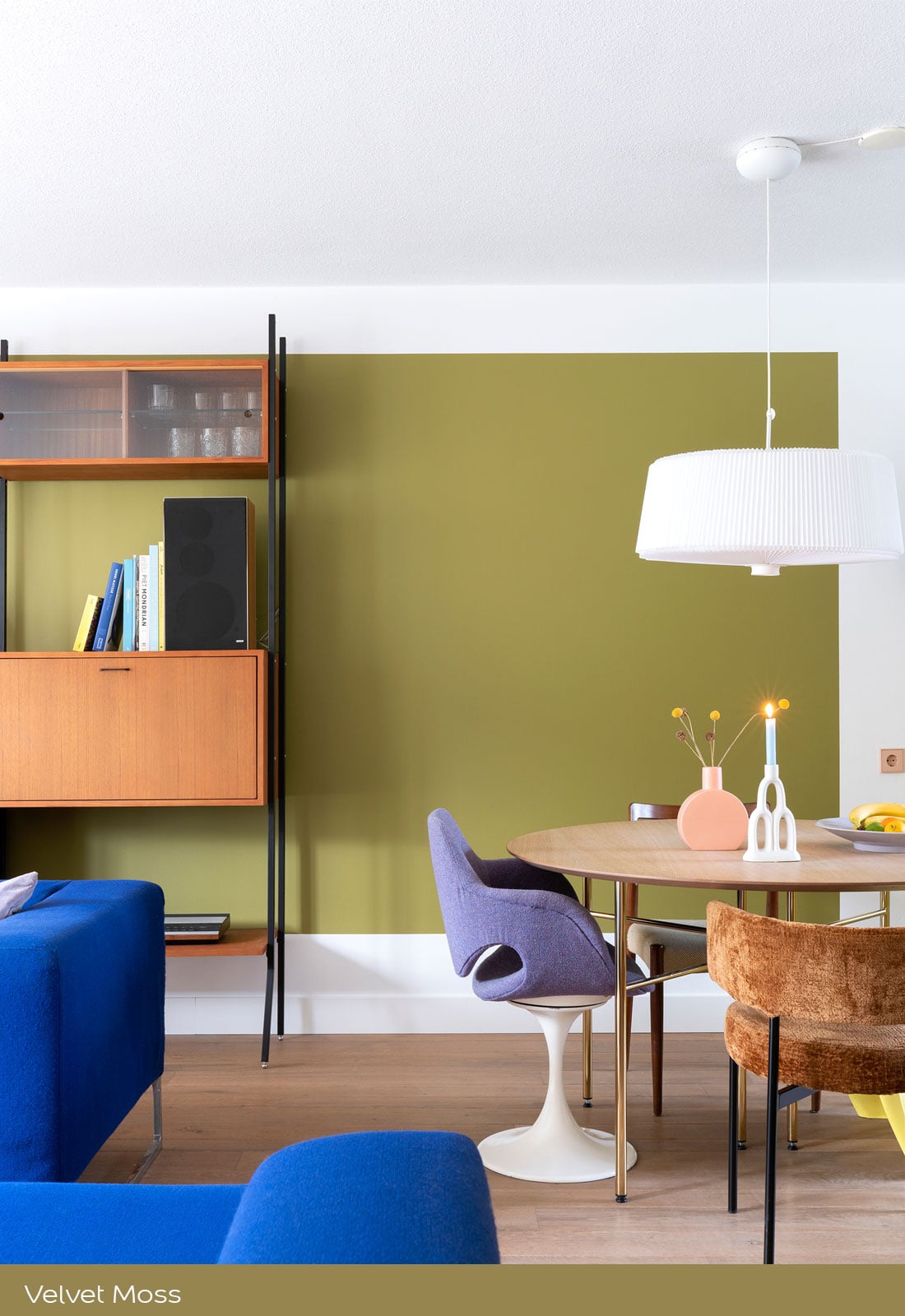 Moderne woon‑eetkamer met groene accentmuur, verschillende stoelen en een blauwe bank