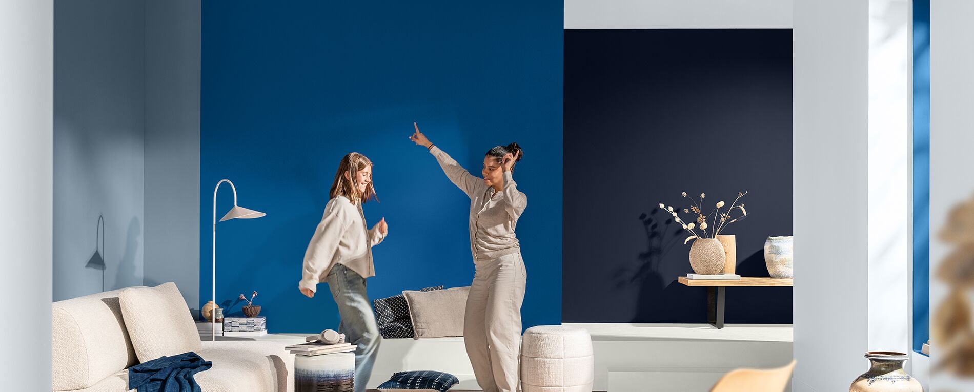 Twee dansende vrouwen in een woonkamer met muren in drie verschillende blauwtinten