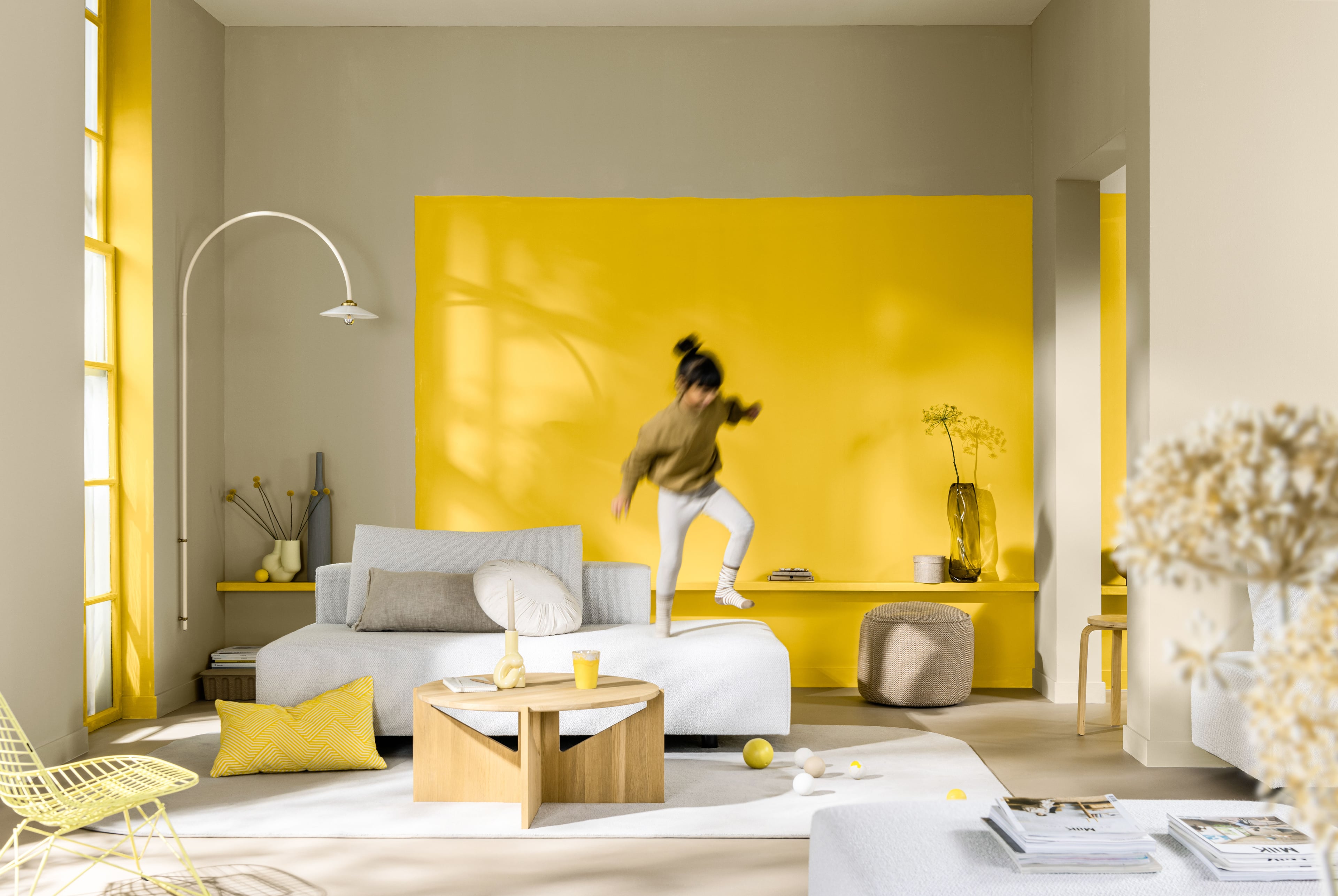 Lichte neutrale woonkamer met zachte meubels en gele accenten.