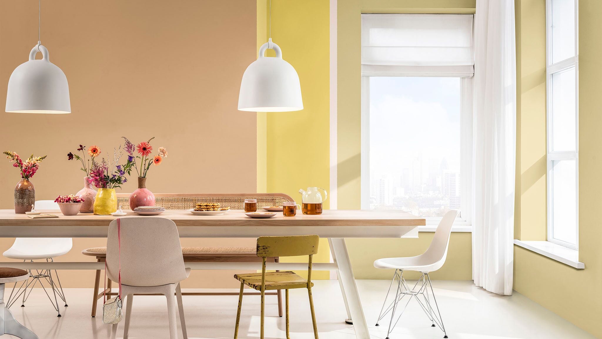 Lichte eetkamer met pastelgekleurde muren, een houten tafel en witte hanglampen.